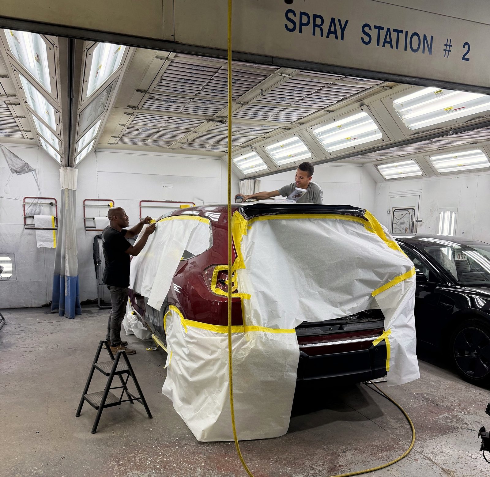 Two of our technicians masking a red SUV for paint in our spray booth